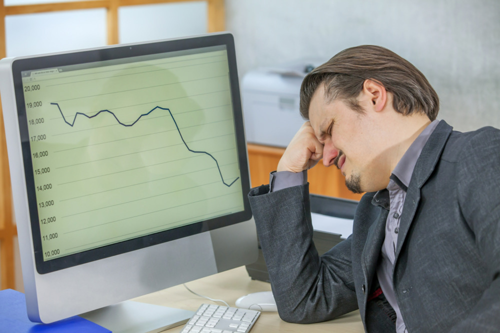 A frustrated businessman looking at a graph showing a downward trend on a computer screen.