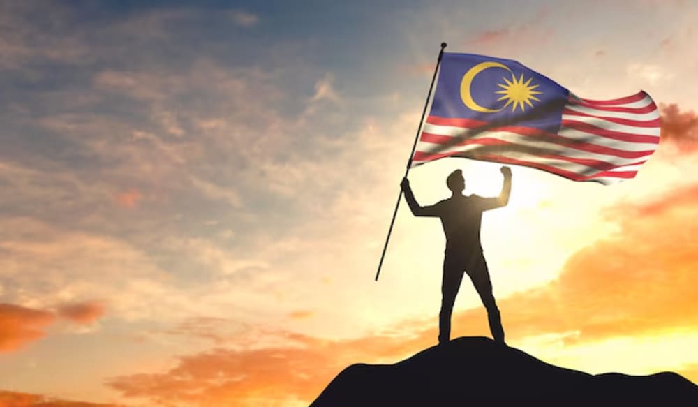 A man standing top of the hill while waving the Jalur Gemilang, Malaysian Flag